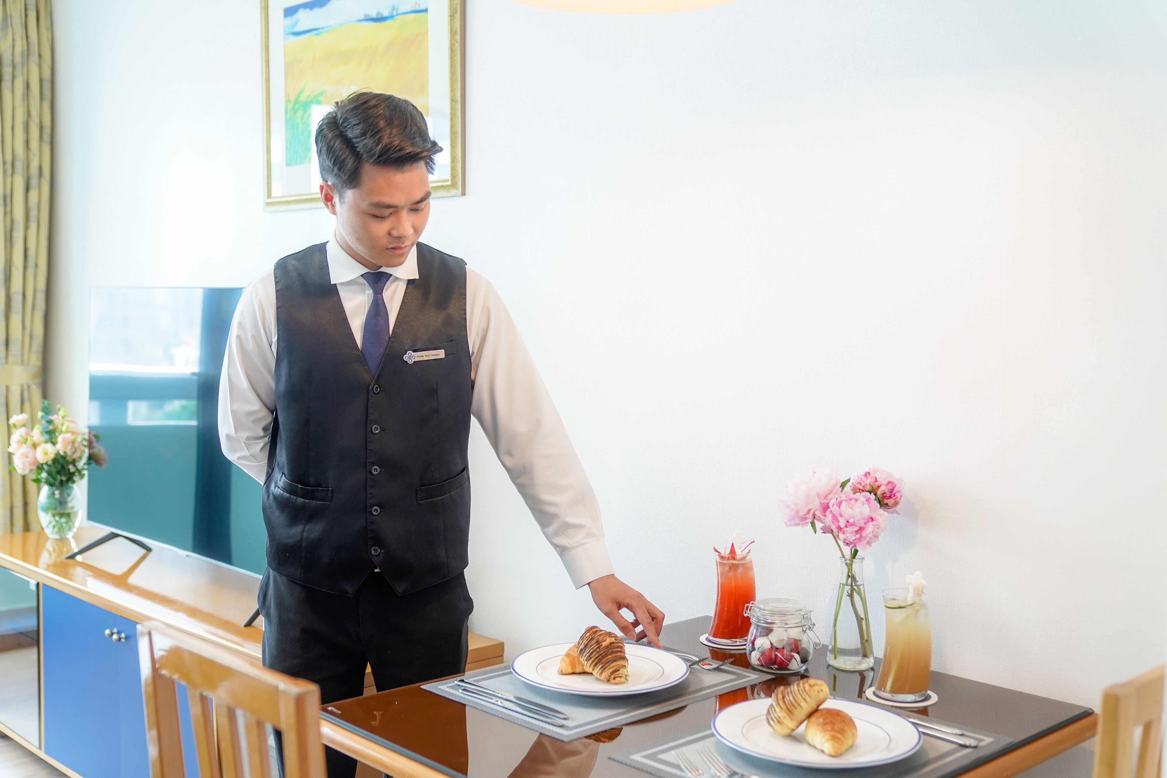 A hotel room with a dining table set for breakfast, including pastries and a glass of juice.