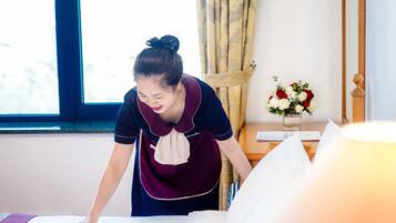 A hotel room with a bed, a window, curtains, a vase with flowers, and a bedside table.