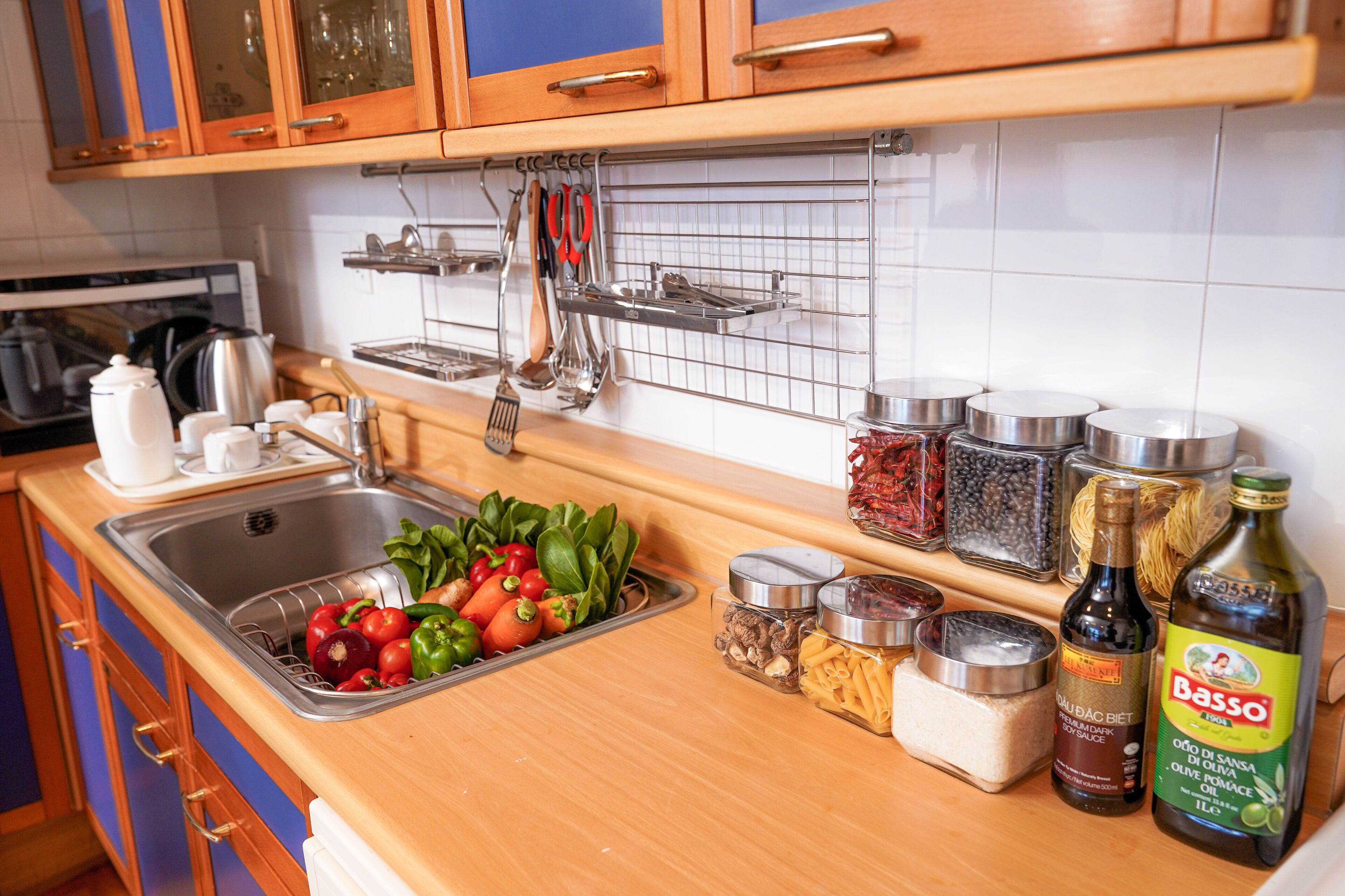 A kitchen with a stainless steel sink, wooden cabinets, and various kitchen utensils and ingredients on the counter.