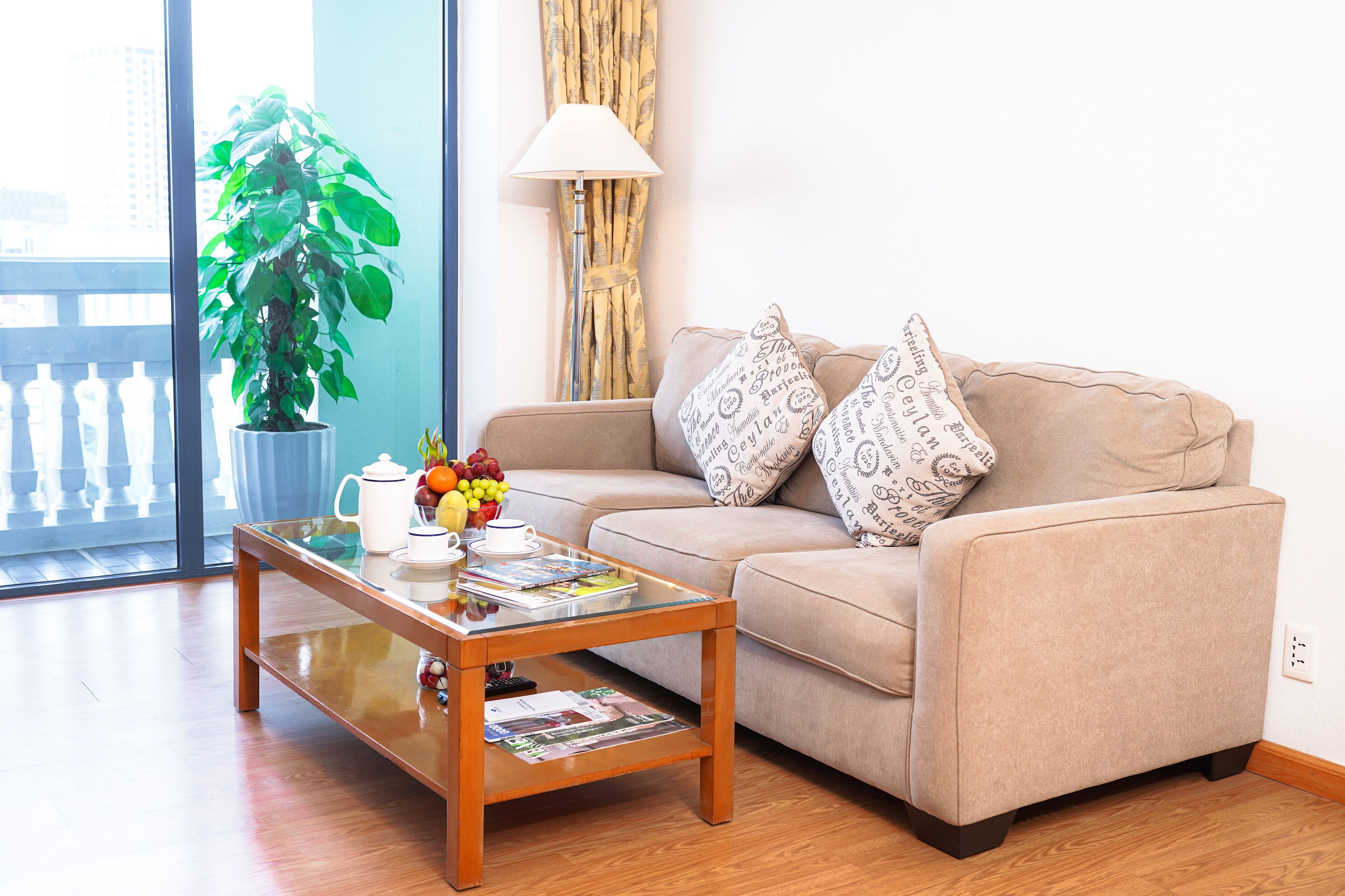 Una sala de estar con sofá, una mesa de centro con revistas, una planta en maceta y una ventana con cortinas.