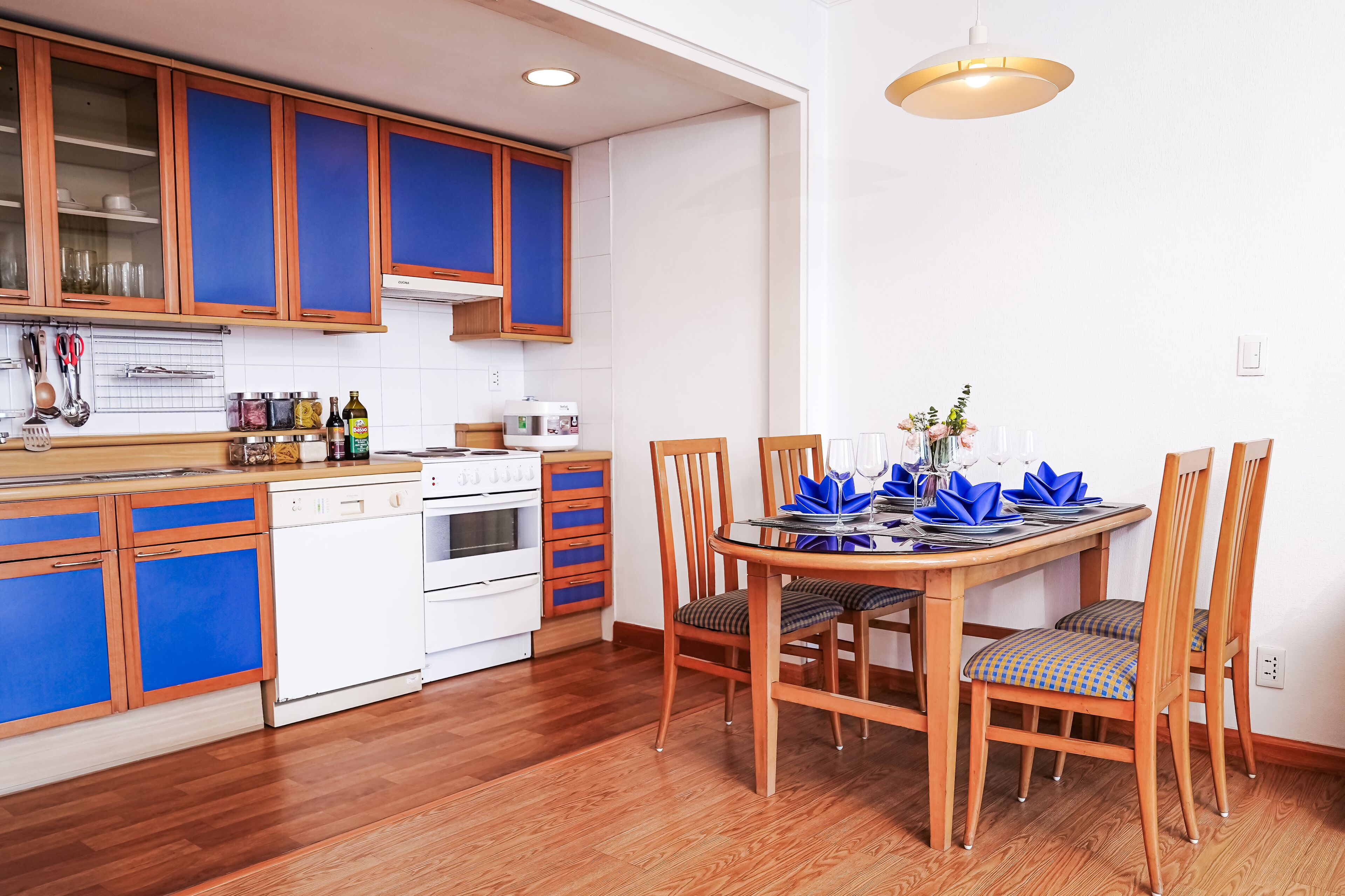 A kitchen with wooden cabinets, a dining table set for two, and a hanging light fixture.