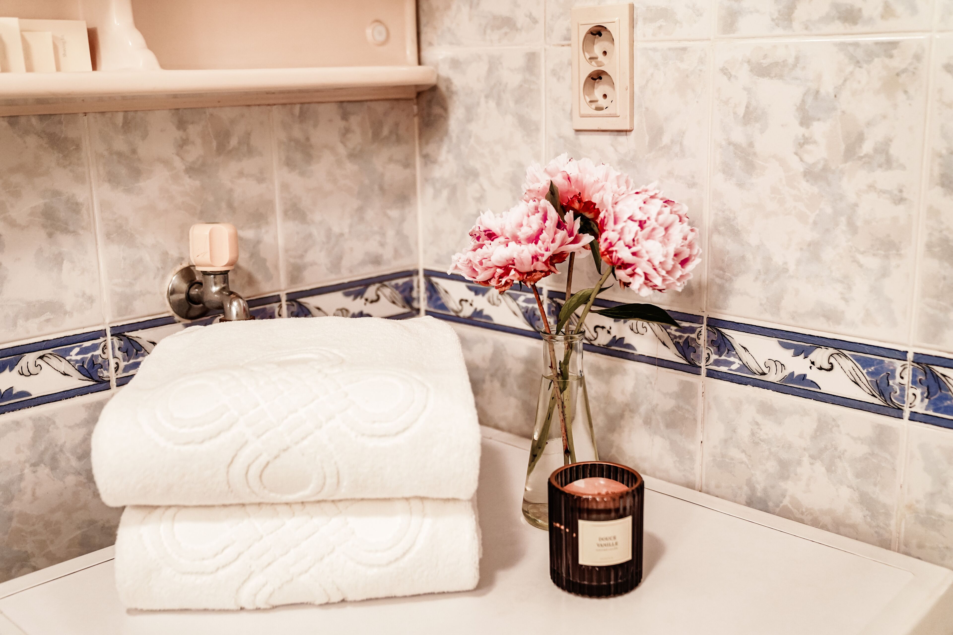 Ein Badezimmer mit einem weißen Handtuch, einer Vase mit rosa Blumen und einer Kerze auf der Ablagefläche.