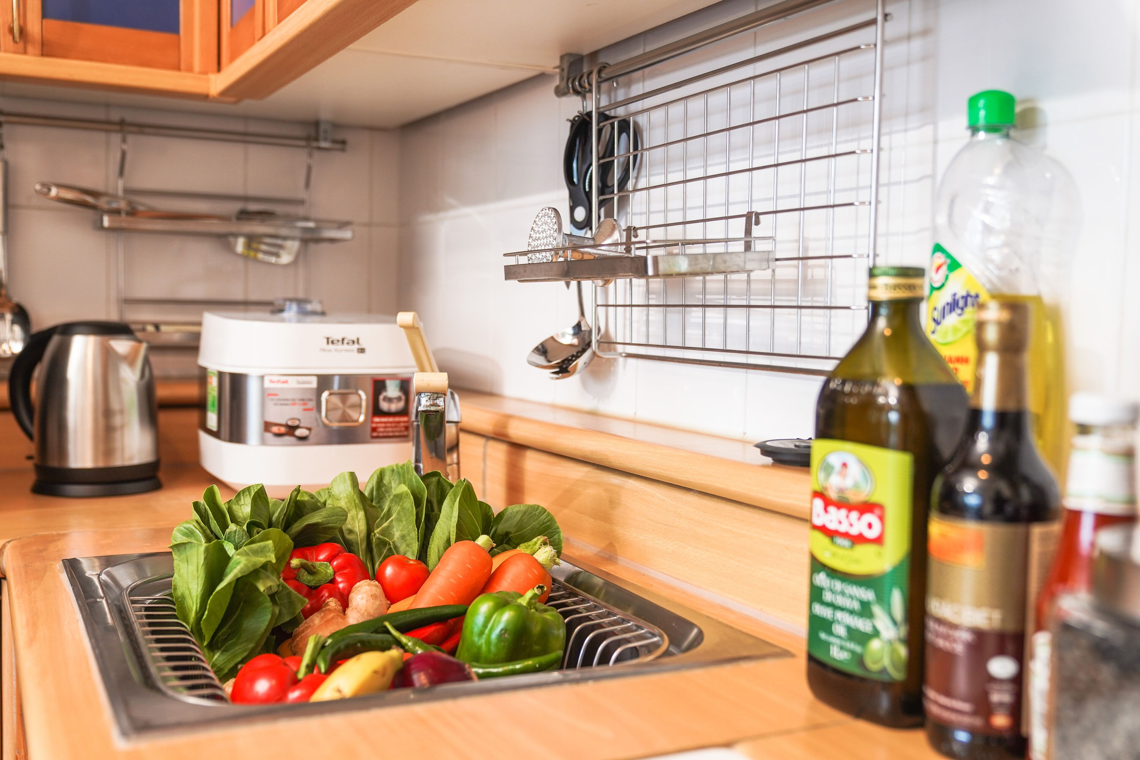 A kitchen with a sink, a kettle, and various bottles and vegetables on the counter.
