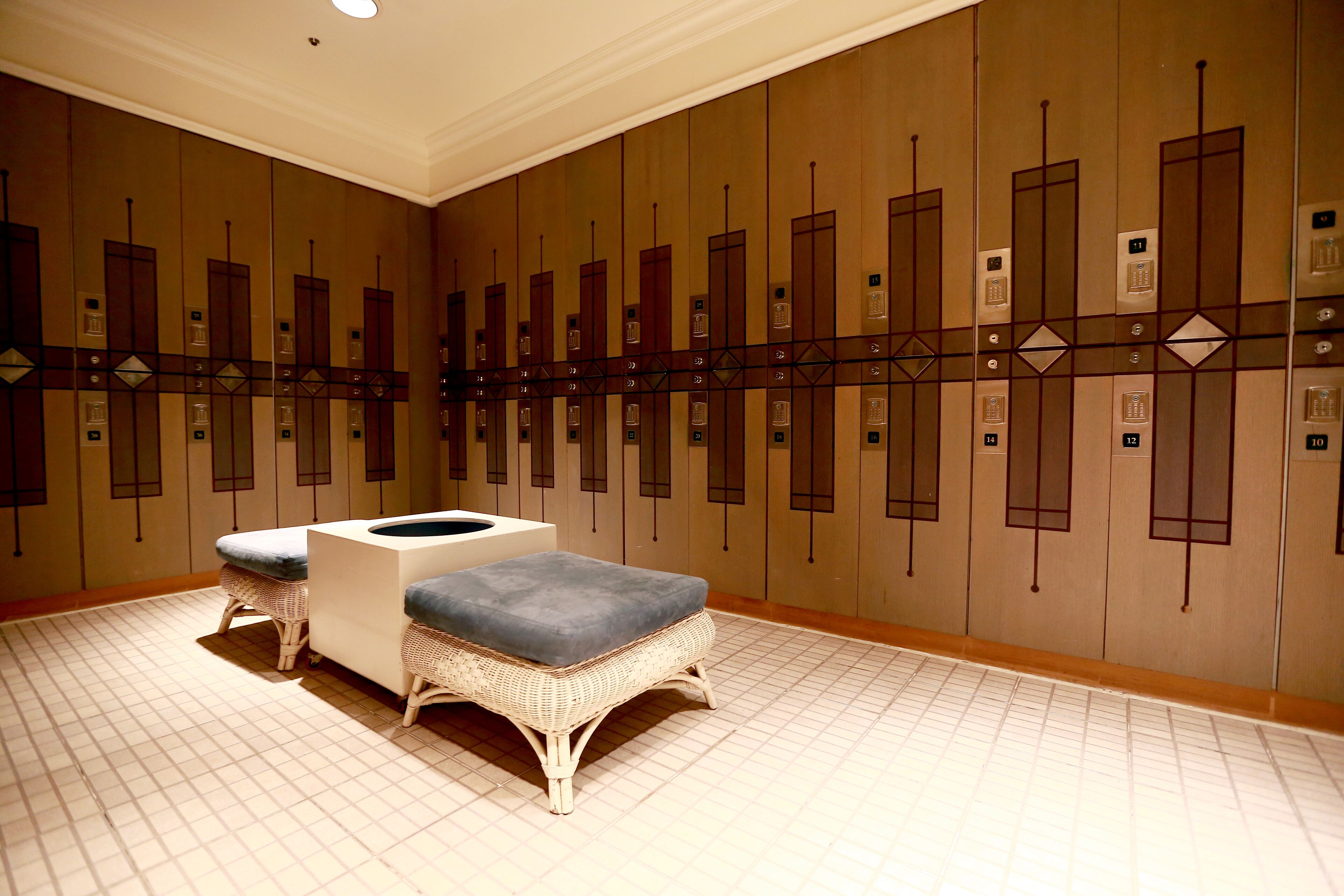 A hotel lobby with a row of lockers, a reception desk, and two wicker chairs with cushions.