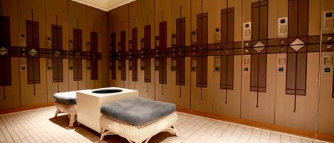 A hotel lobby with a row of lockers, a reception desk, and two wicker chairs with cushions.