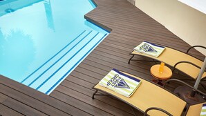 Un espace piscine doté d’une terrasse en bois, de chaises longues et d’une table avec des boissons.