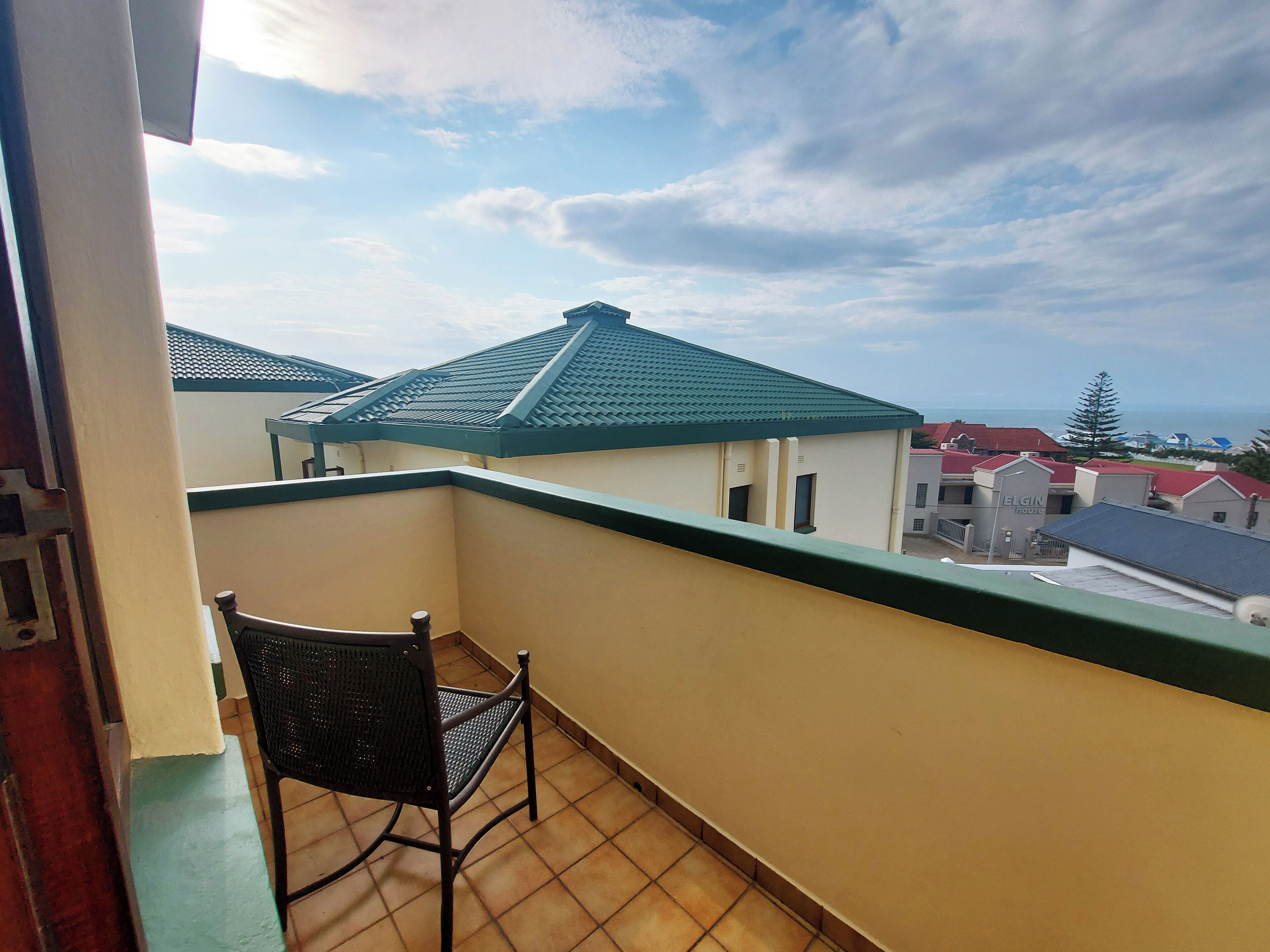Un balcone con una sedia, vista su edifici dai tetti verdi e cielo sereno.