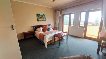 Habitación de hotel con cama, ventilador de techo, un cuadro, una ventana y vistas al exterior.