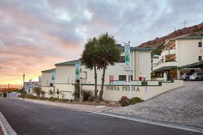 A hotel named 'PERNA PERNA' with a prominent entrance, palm trees, and a mountainous backdrop.