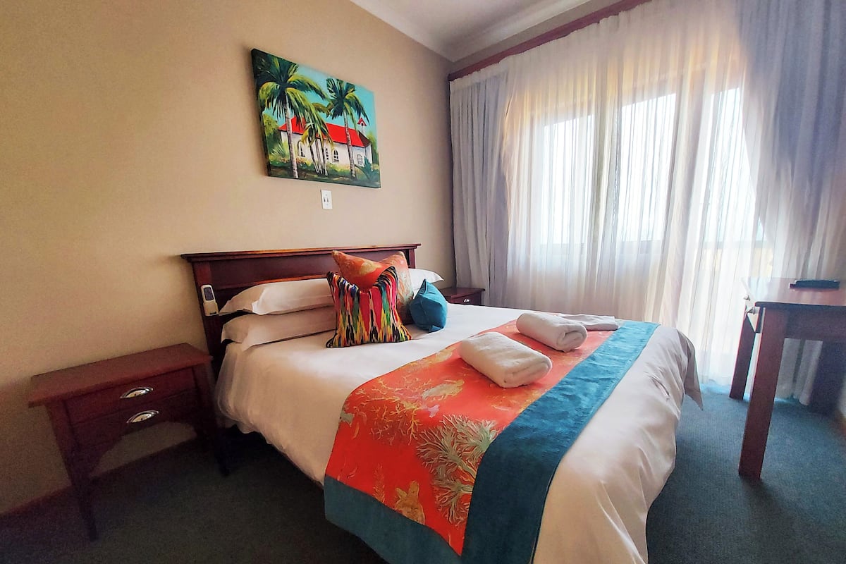 A hotel room with a bed, a nightstand, a desk, and a painting on the wall.