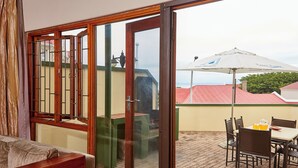 Une pièce dotée d’une porte-fenêtre coulissante donnant sur une terrasse extérieure avec une table, des chaises et un parasol.
