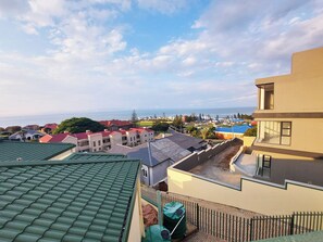 A residential area with a view of the sea, featuring houses with red and grey roofs, a yellow building, and a green roof.