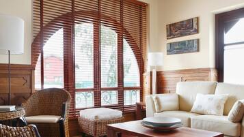 A living room with a sofa, a coffee table, wicker chairs, a lamp, and a large window with wooden blinds.