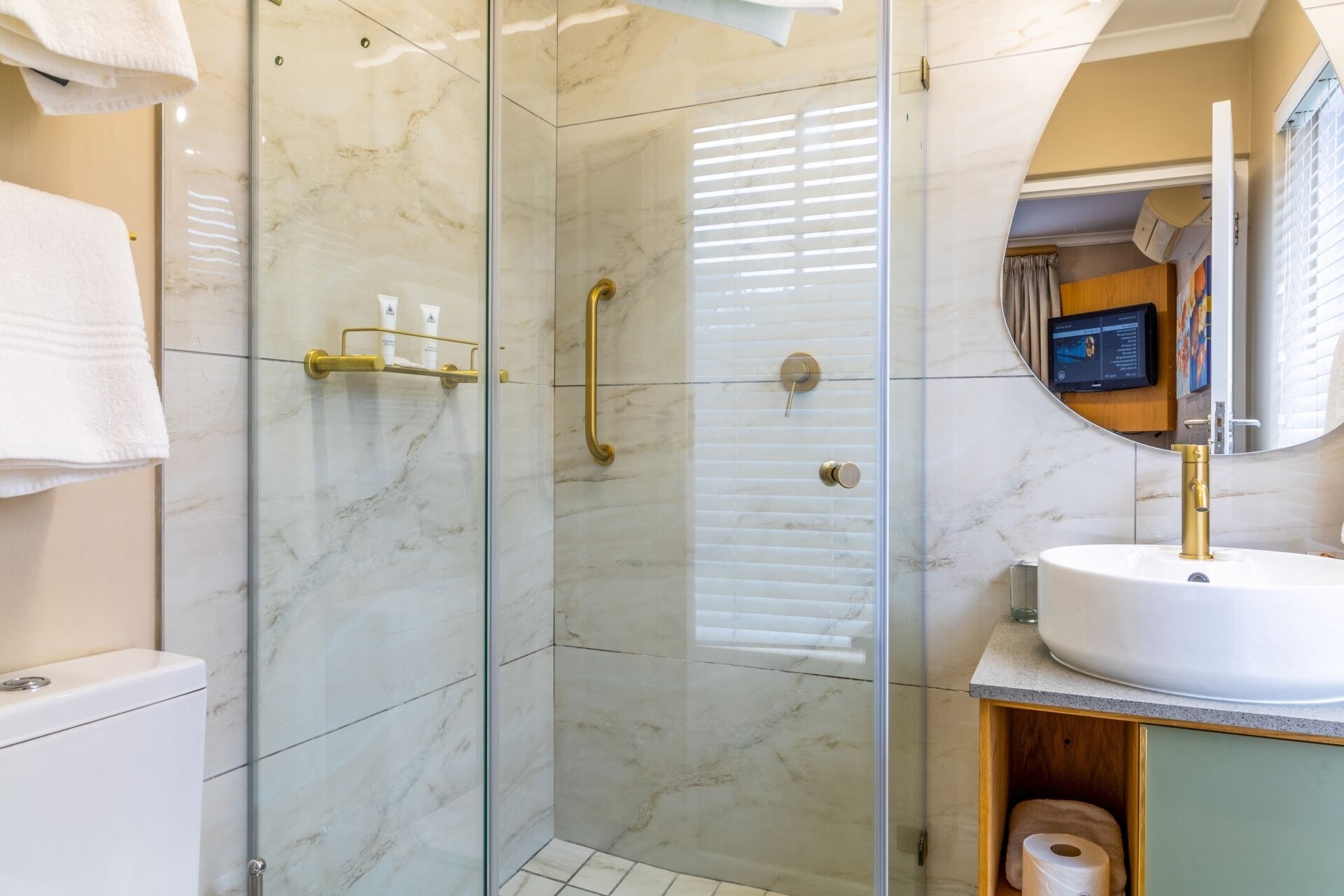 Ein modernes Badezimmer mit einer in Glas eingefassten Dusche, einem weißen Waschbecken mit goldfarbenem Wasserhahn und einem Spiegel über dem Waschbecken.