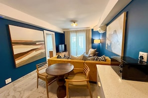 A hotel room with a sofa, dining table, chairs, a TV, and artwork on the walls. - First Group Hastings Hall (Cape Town)