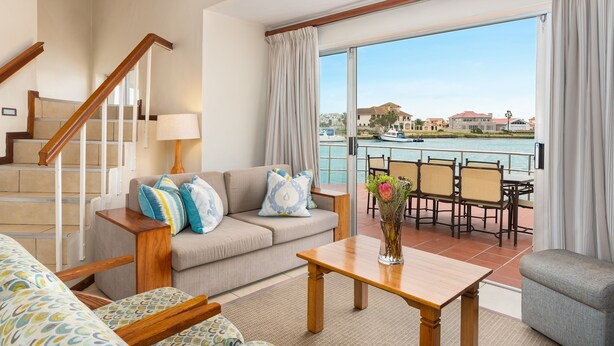 A spacious living room with a sofa, a coffee table, and a view of a marina. - First Group Port Owen Marina (Bergrivier)