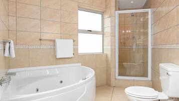 A modern bathroom with a large bathtub, a glass-enclosed shower, and a toilet.