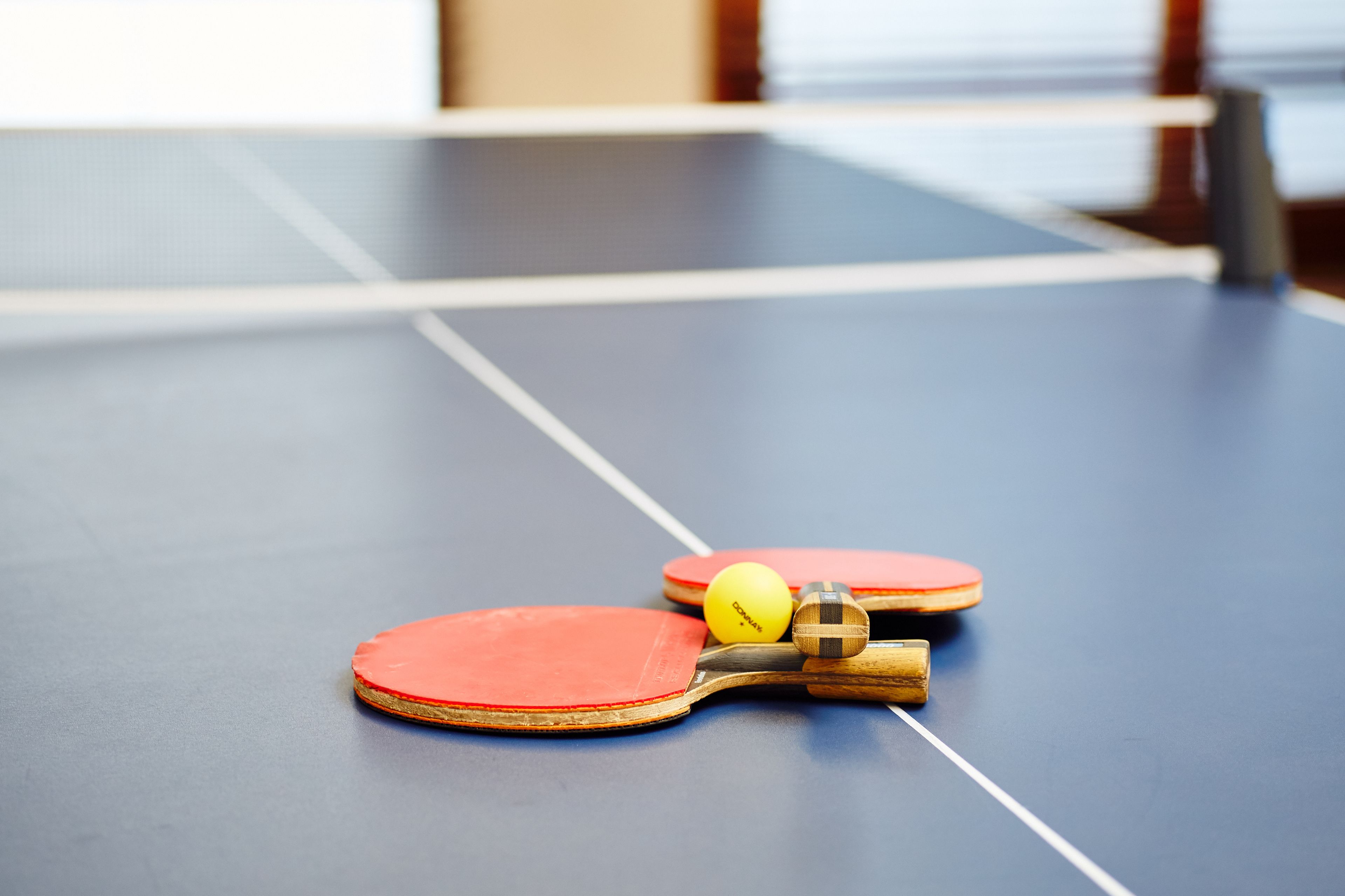 A table tennis table with two red paddles and a yellow ball.