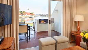 A hotel room with a balcony, a TV, a table with a lamp, and a view of a pool and buildings. - First Group Port Owen Marina (Bergrivier)