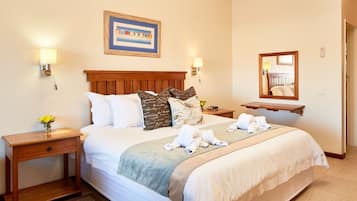 A neatly made bed with a wooden headboard, a bedside table with a lamp, a mirror, and a framed picture on the wall.