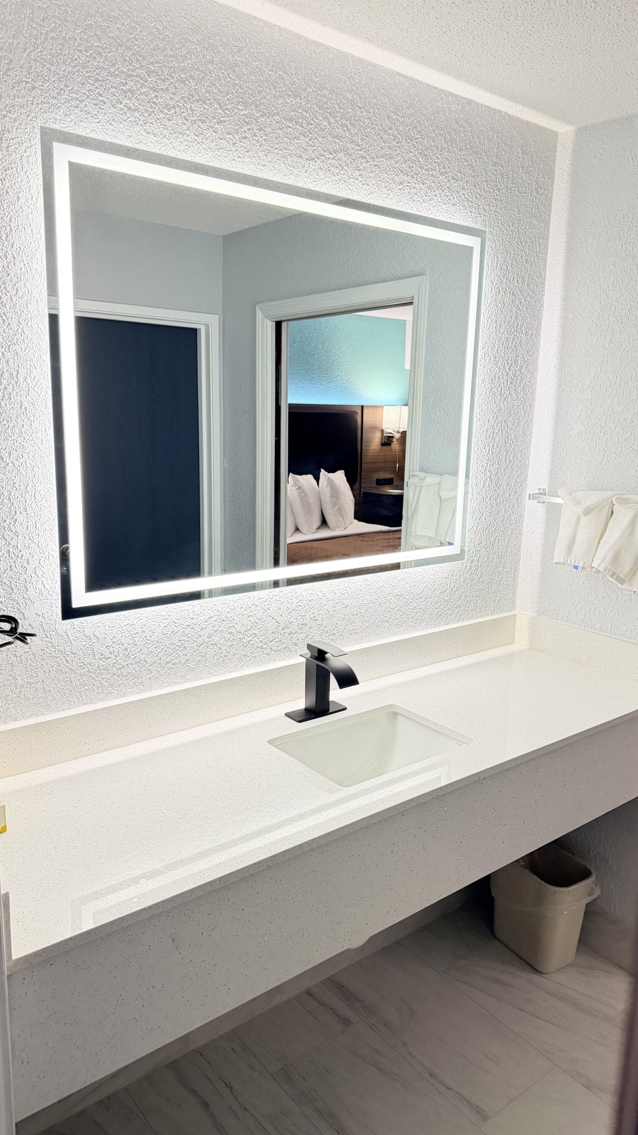 A bathroom with a large mirror, white countertop, and a sink.