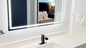 A bathroom with a large mirror, white countertop, and a sink.