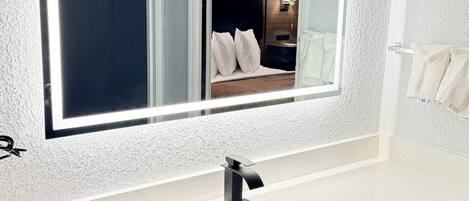 A bathroom with a large mirror, white countertop, and a sink.