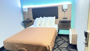 Habitación de hotel con cama, mesita de noche, lámpara de pared y puerta con pomo.