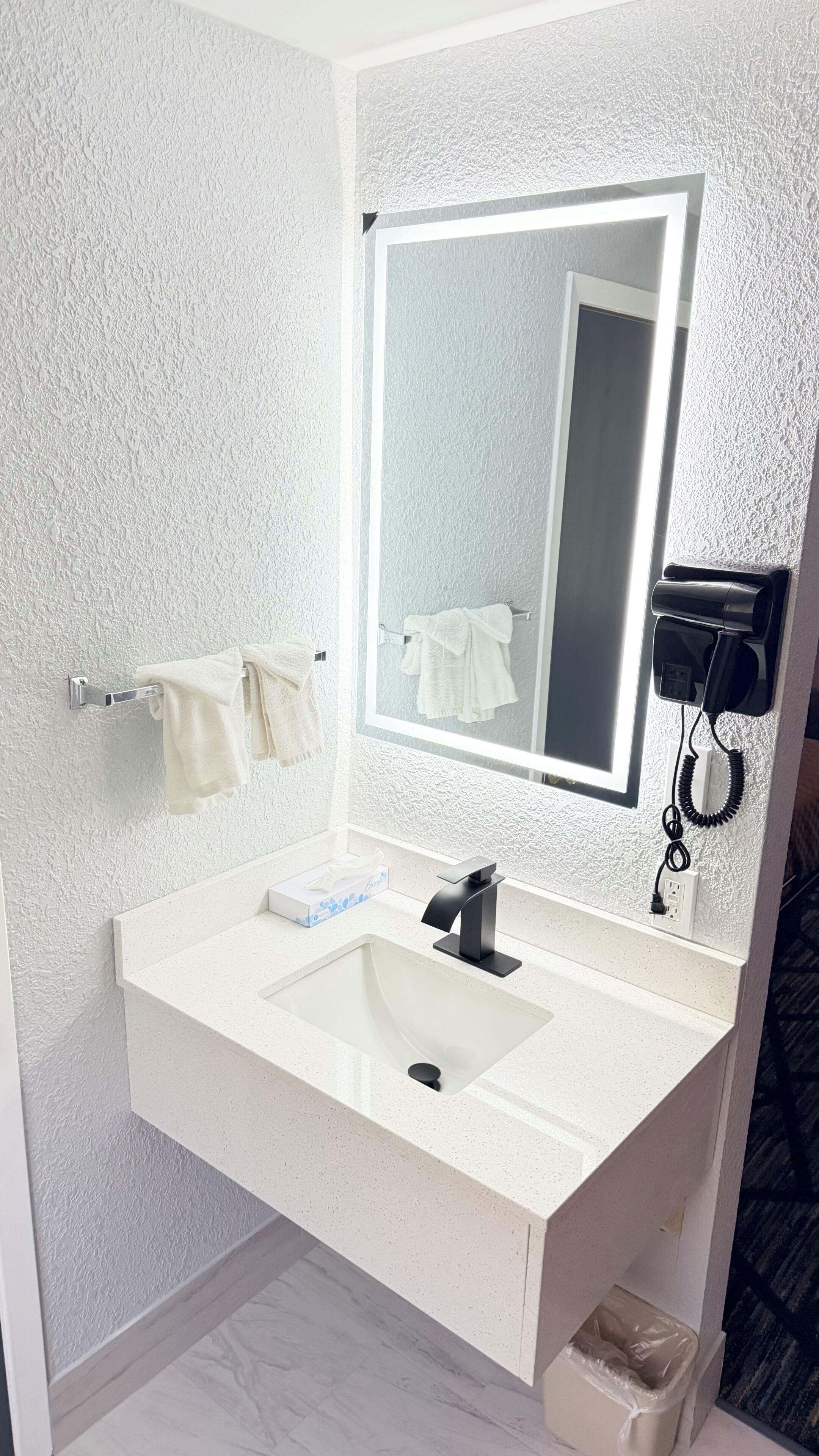 A bathroom with a white sink, a mirror, a towel rack, and a hairdryer.