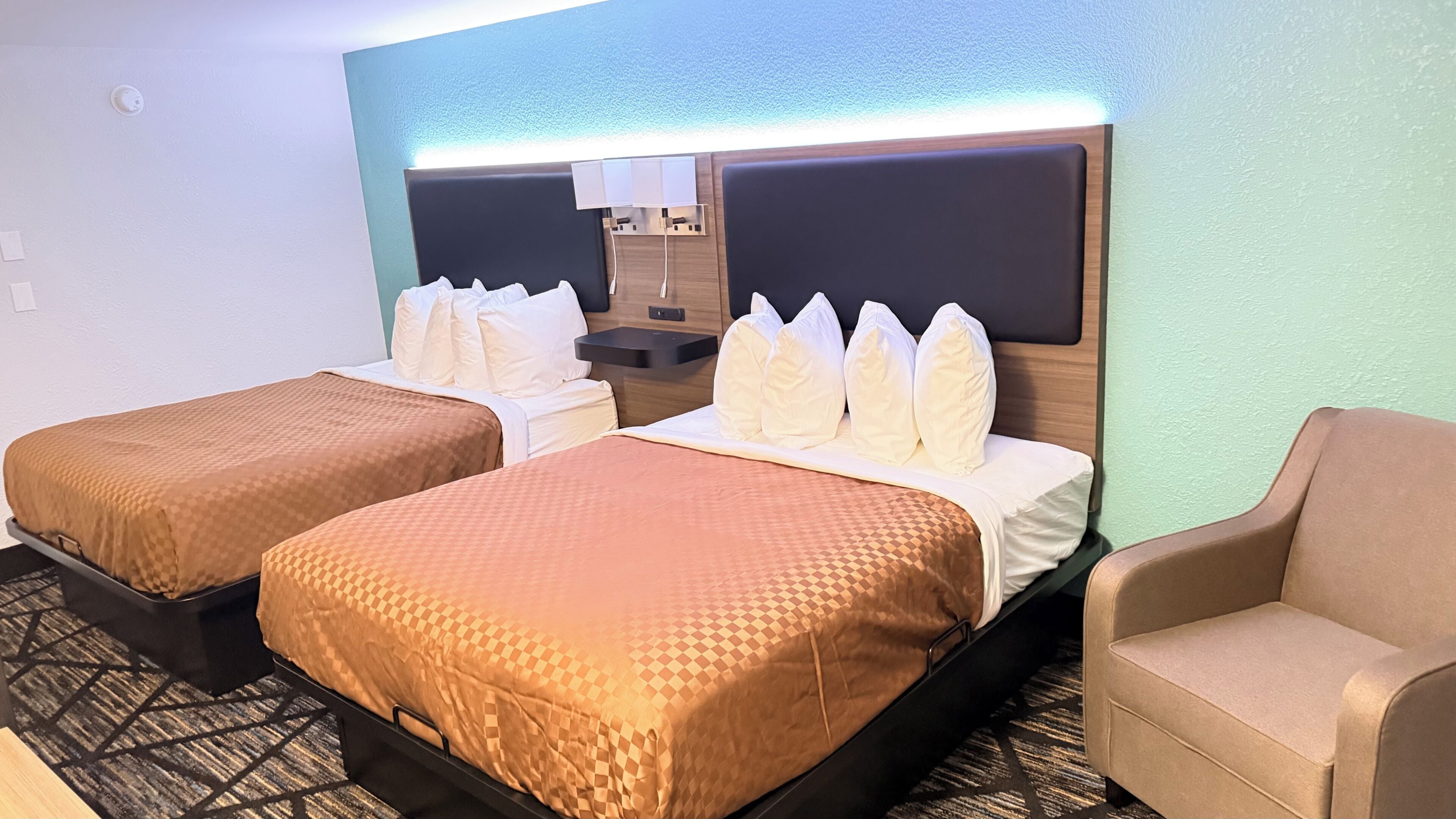 A hotel room with two beds, a small desk, a chair, and a mirror.