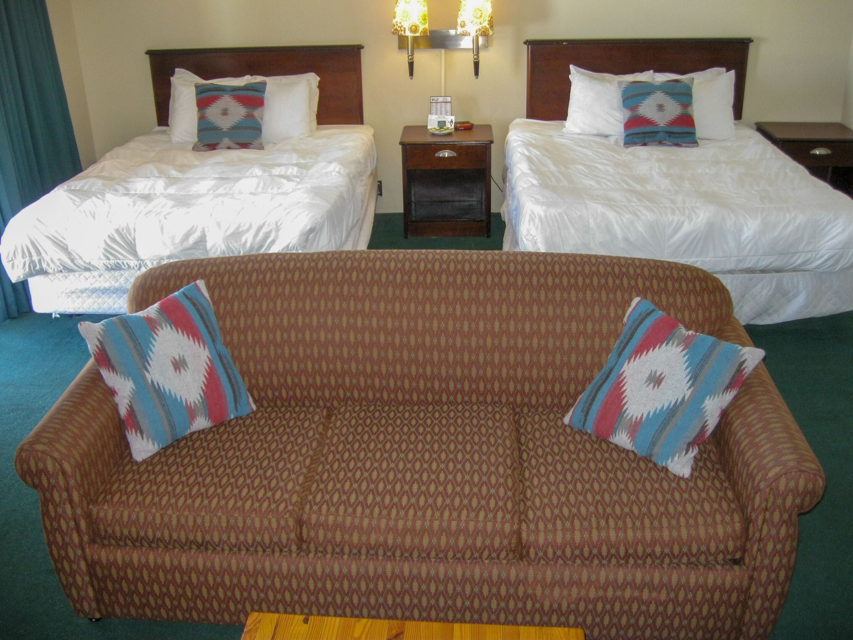 A hotel room with two beds, a brown sofa, and a small wooden table.