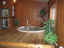 Un espacio de spa de madera con un jacuzzi, un reloj y plantas en macetas.