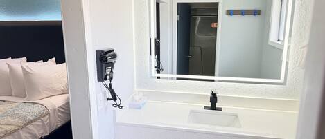 A hotel room with a bed, a bathroom with a sink and mirror, and a hairdryer on the wall.