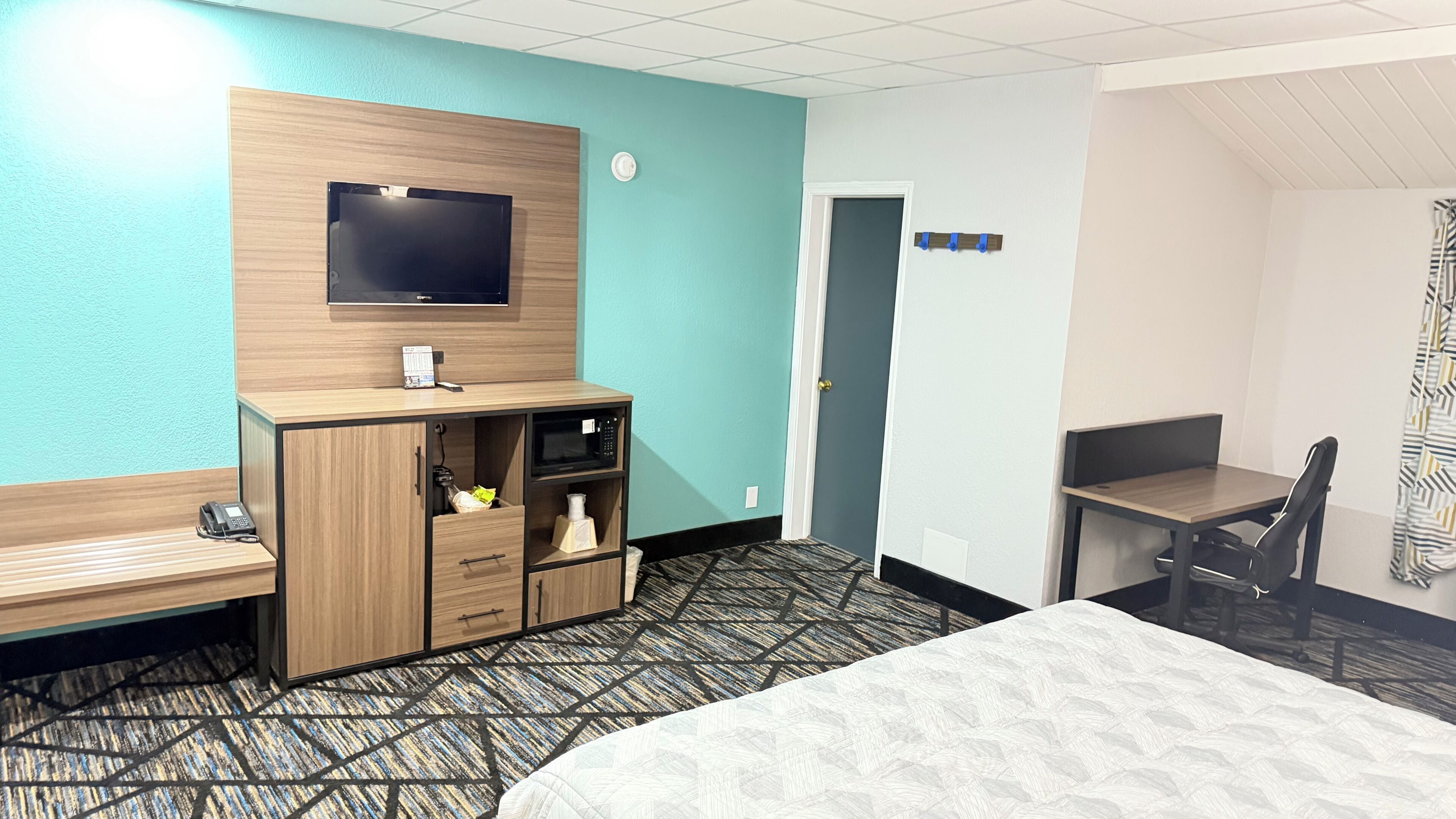 A hotel room with a bed, a desk, a television, a minibar, and a door.