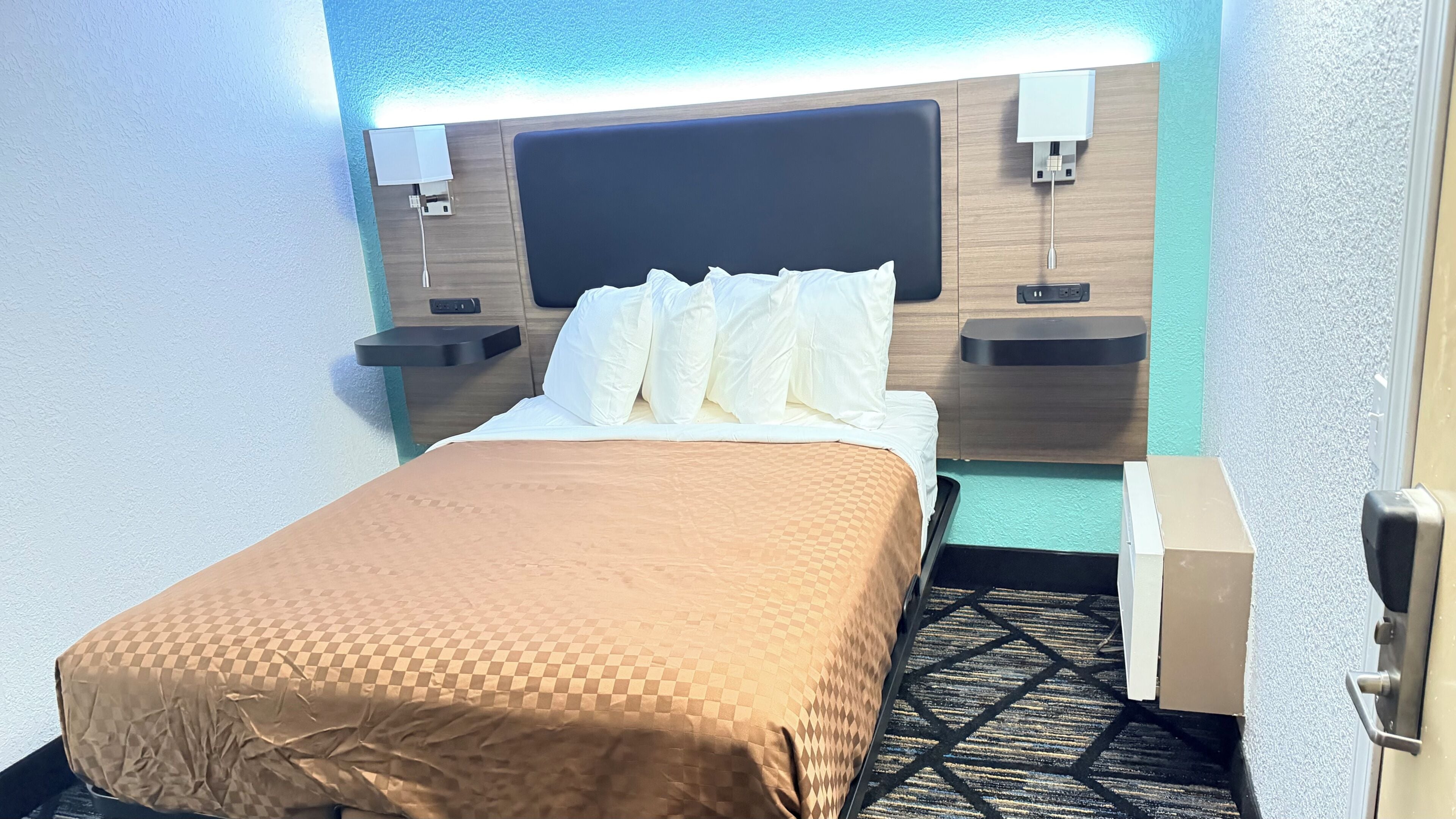 Une chambre d’hôtel comprenant un lit, des tables de chevet, une petite table et un luminaire fixé au mur.