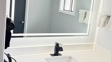 A bathroom with a white sink, a mirror, and a window.