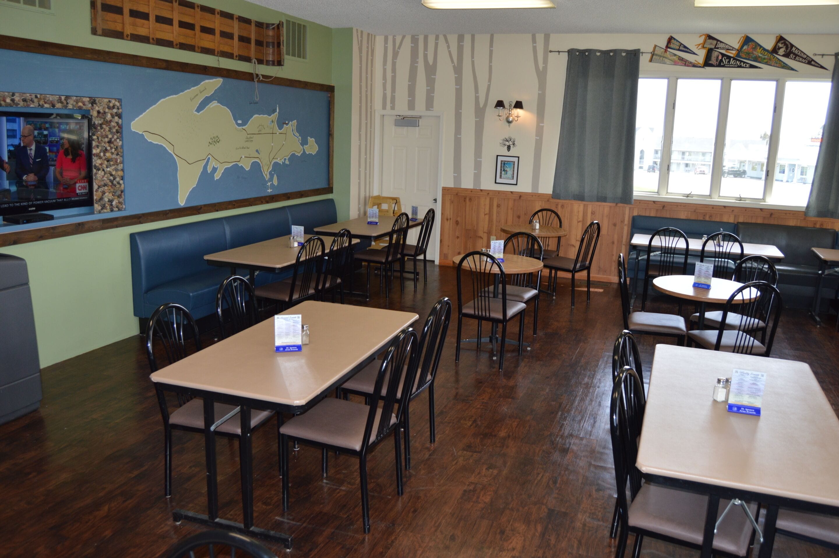 A restaurant with booths, tables, and chairs. There is a map on the wall and a TV screen displaying a news program.