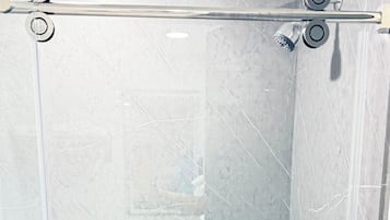 A glass-enclosed shower stall with a chrome shower head and handle, a visible drain, and a tiled wall.