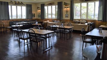 Un comedor con varias mesas y sillas, pisos de madera y ventanas grandes con cortinas.