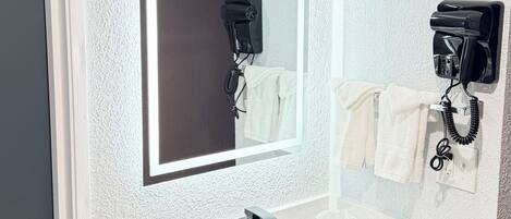 Un baño con un lavamanos blanco, un espejo y dos secadores de pelo montados en la pared.