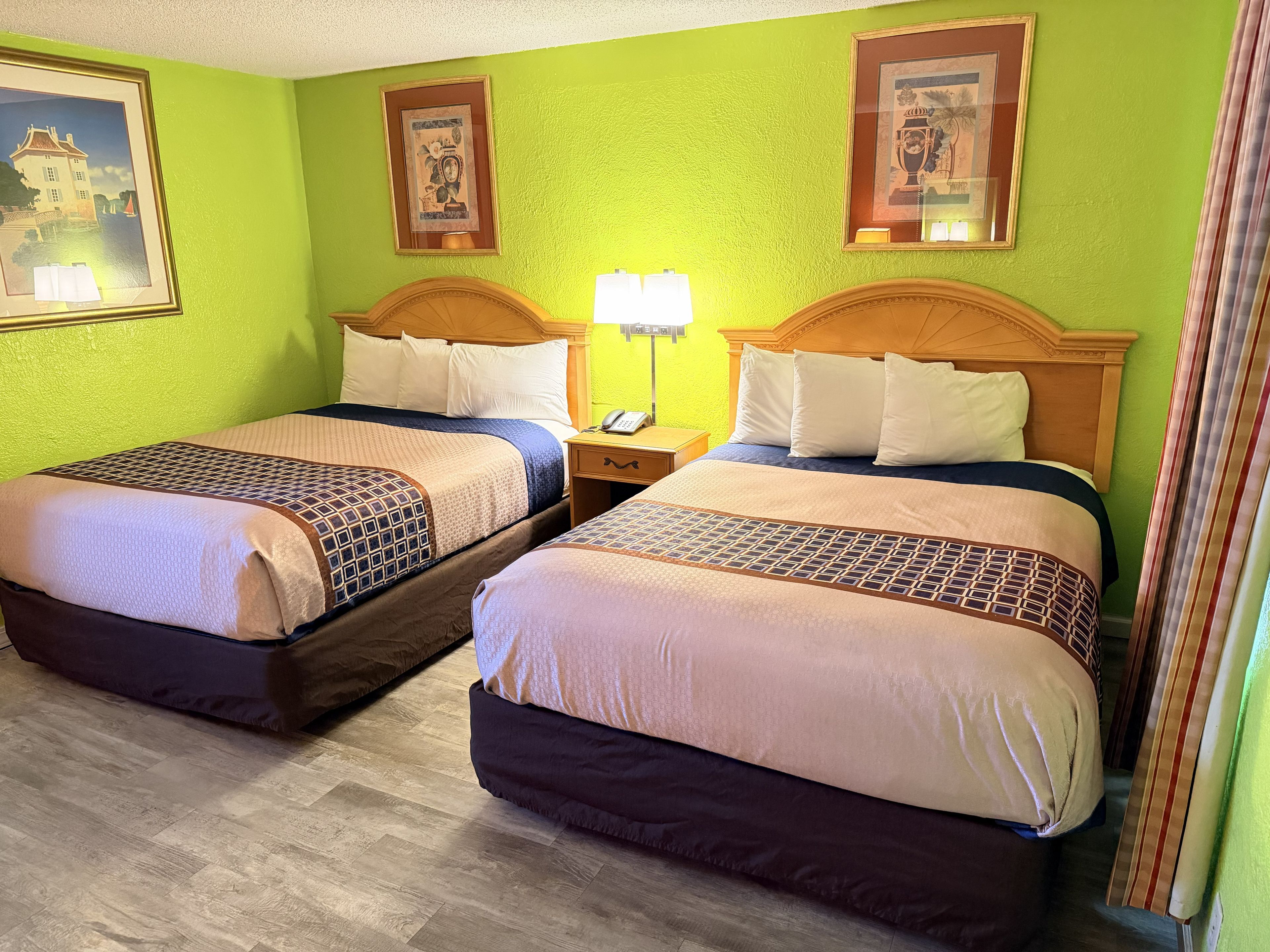 Una habitación de hotel con dos camas, una mesita de noche con lámpara y obras de arte en las paredes.
