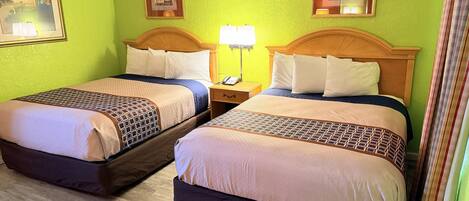 A hotel room with two beds, a nightstand with a lamp, and artwork on the walls.