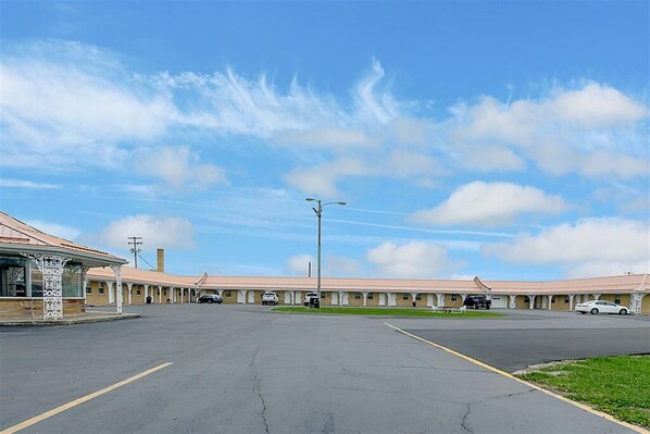 A motel with a row of rooms, a parking lot, and a small building with a covered area.