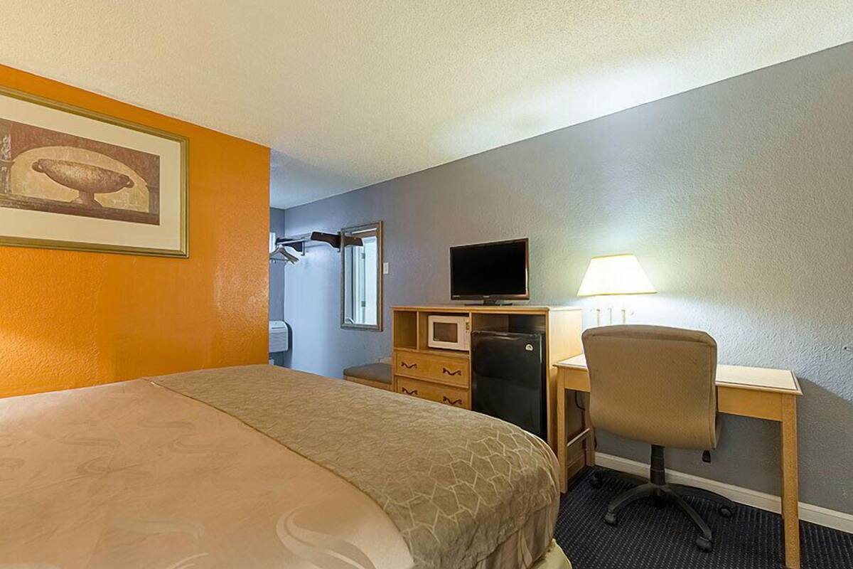 Une chambre d’hôtel équipée d’un lit, d’un bureau avec un ordinateur, d’une chaise, d ’une télévision et d’un four à micro-ondes.