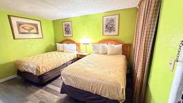 A hotel room with two beds, a wooden headboard, a nightstand with a lamp, and a green wall.