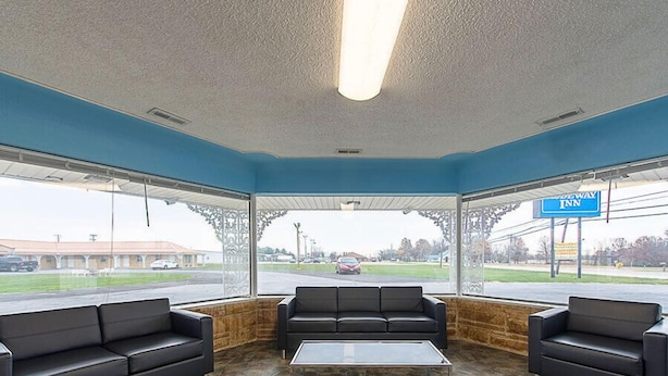 A motel lobby with a stone floor, black leather couches, and a large window offering a view of the road and a building in the distance. - Highway Inn (Paris)