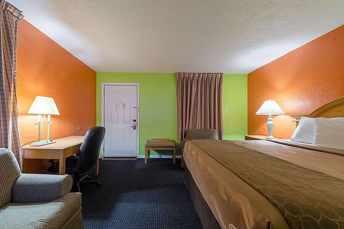 Une chambre d’hôtel avec un lit, un bureau doté d’une lampe, une chaise et une petite table.