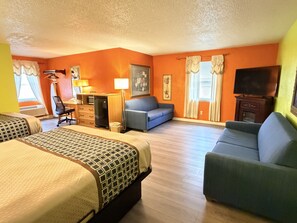 A hotel room with a bed, two sofas, a desk, a television, and a window with curtains.