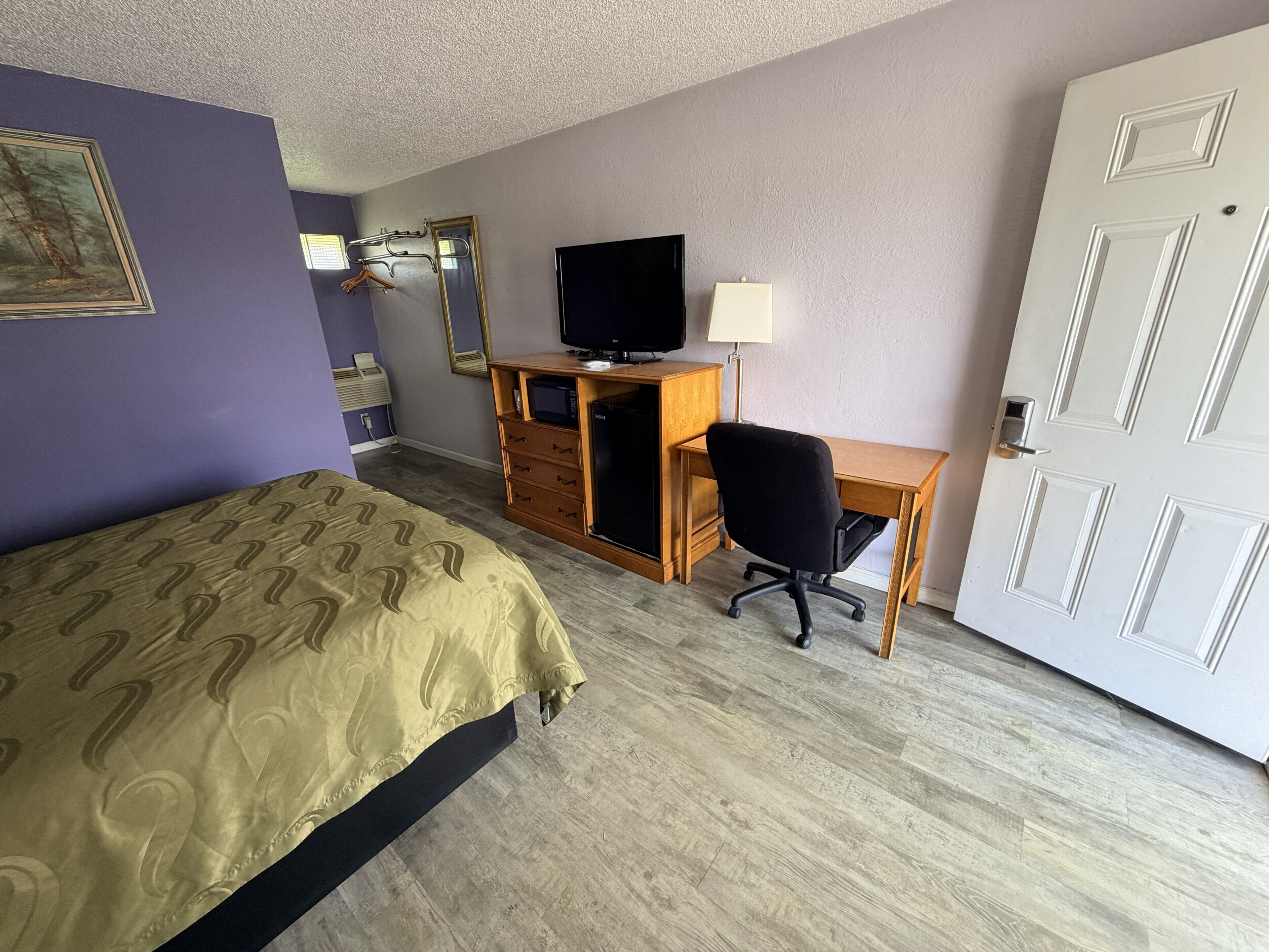 Habitación de hotel con cama, escritorio, silla, televisor y puerta.