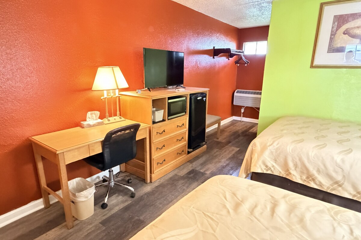 Une chambre d’hôtel avec un bureau en bois, une chaise, un lit, une télévision et un radiateur fixé au mur.